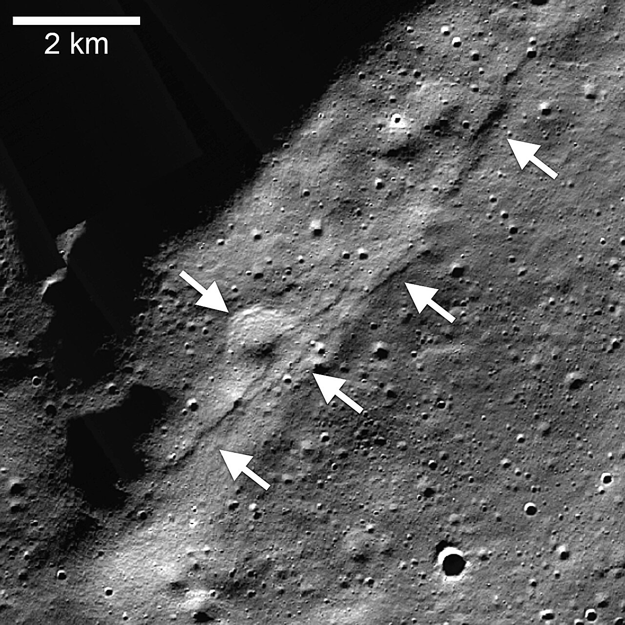 Mosaico da Lunar Reconnaissance Orbiter Camera (LROC), Narrow Angle Camera (NAC) do conjunto Wiechert de escarpas lobadas (setas apontando para a esquerda) próximo ao polo sul lunar. Uma escarpa de falha de empuxo cortou uma cratera degradada de aproximadamente 1 quilômetro (0,6 milha) de diâmetro (seta apontando para a direita)